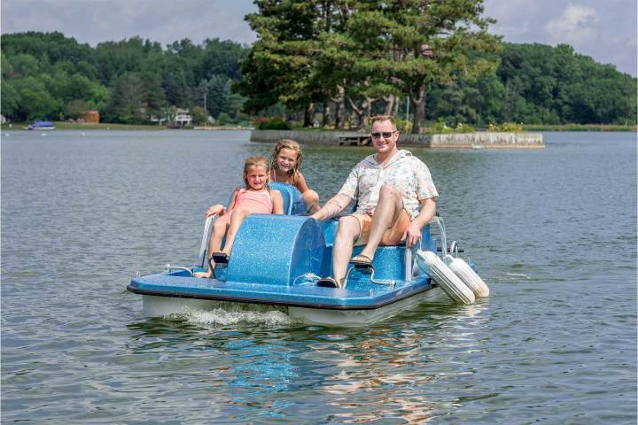 a man riding on the back of a boat next to a lake